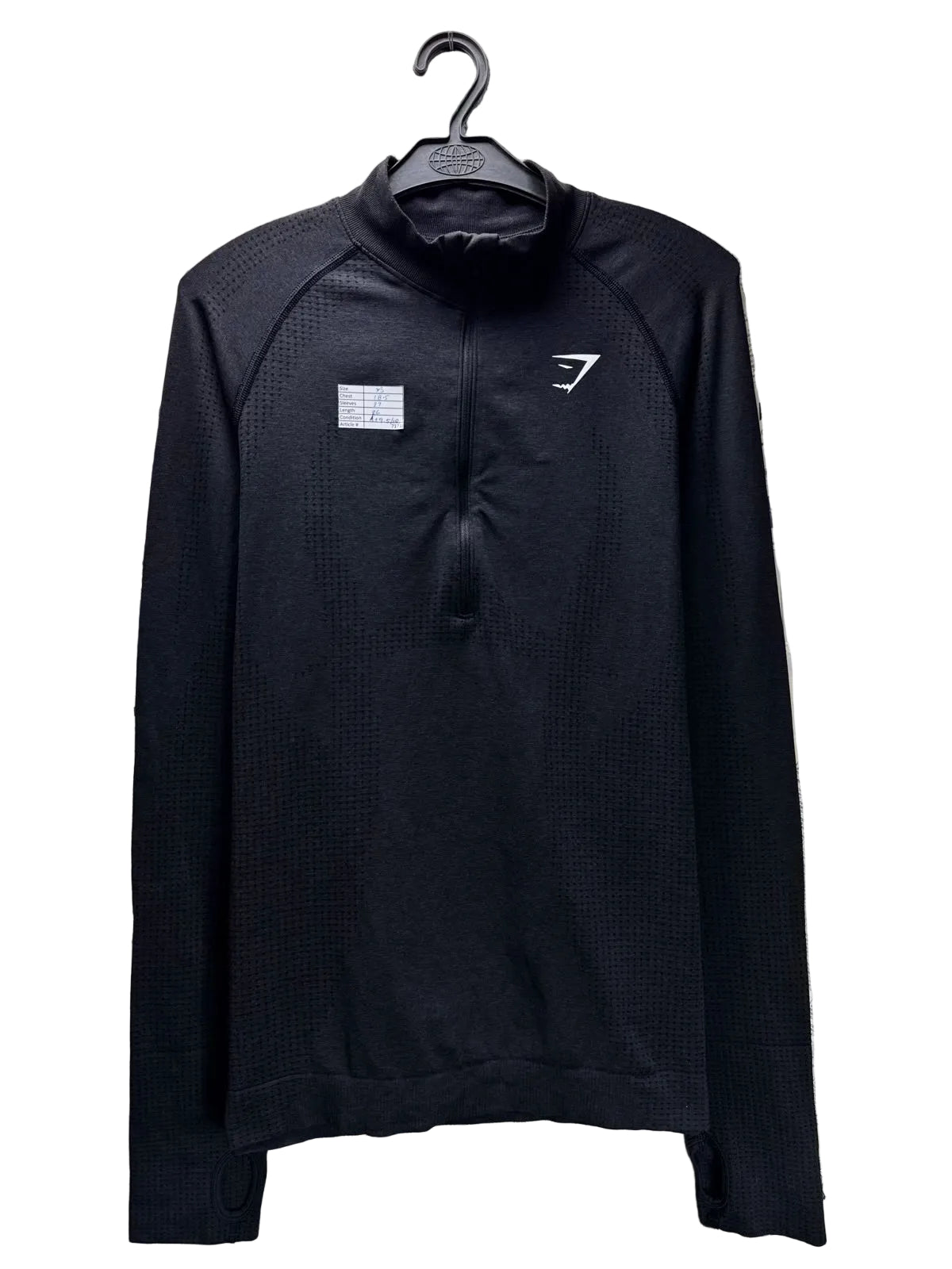 A black long-sleeve quarter-zip athletic pullover with a textured waffle knit pattern, hanging on a black hanger against a background of printed newspaper pages. The left chest features a small white rectangular patch, and the right chest features a white stylized logo.