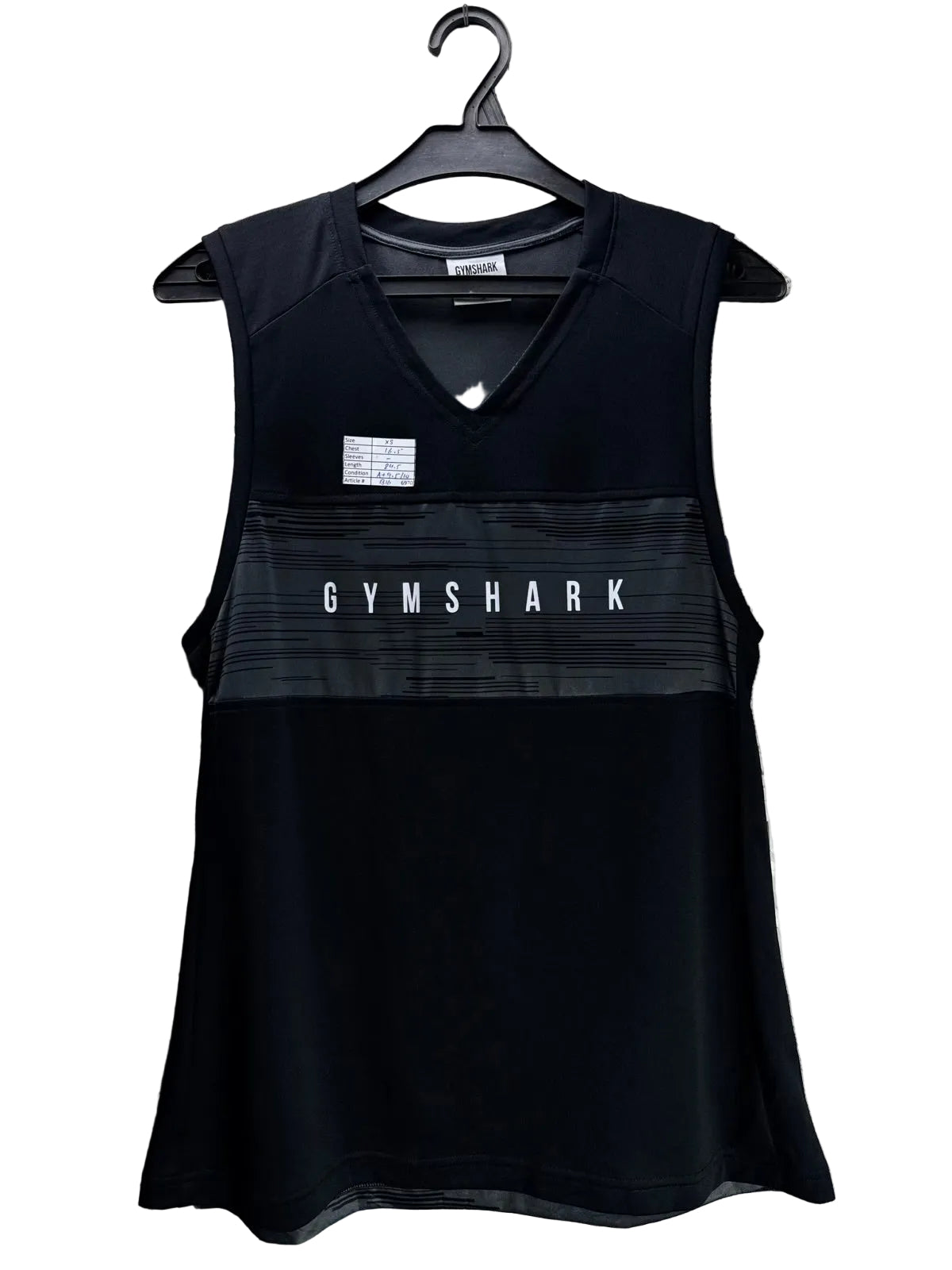 Black Gymshark sleeveless athletic tank top hanging on a black hanger against a background of printed newspapers. The top features a V-neck, a horizontal textured stripe across the chest with 'GYMSHARK' printed in white, and a small white brand patch on the upper left chest.