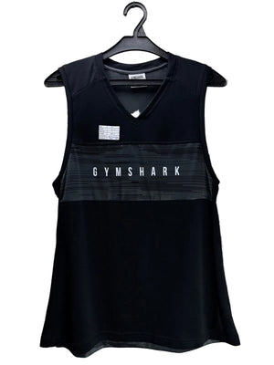Black Gymshark sleeveless athletic tank top hanging on a black hanger against a background of printed newspapers. The top features a V-neck, a horizontal textured stripe across the chest with 'GYMSHARK' printed in white, and a small white brand patch on the upper left chest.