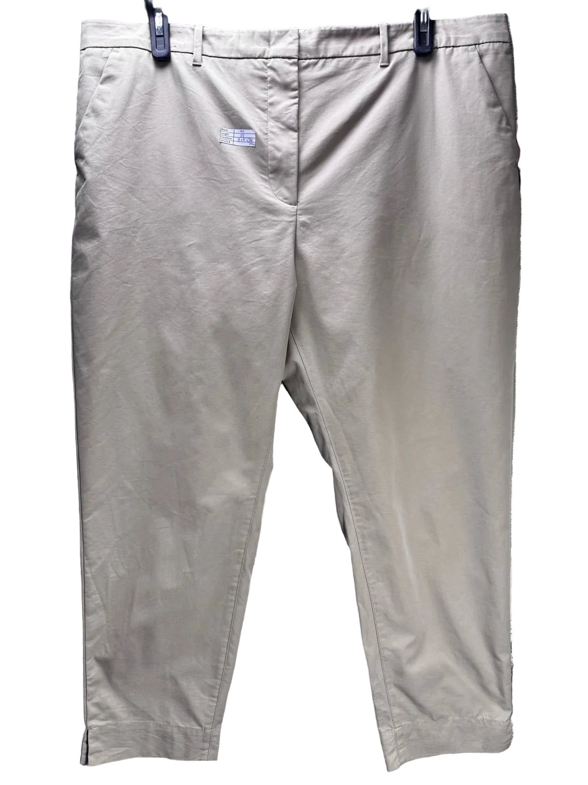 A pair of light beige chino pants hanging on a black hanger against a background of newspaper pages.